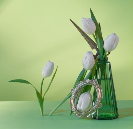 white tulips in green glass vase on green background
