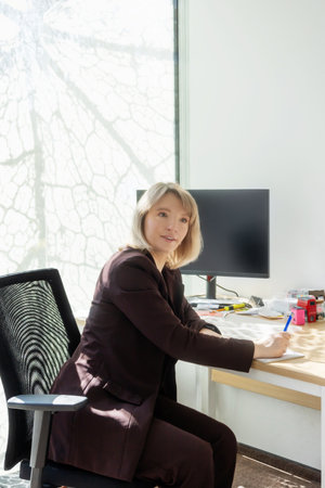 woman in suit writing at desk in officeの写真素材