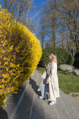 blonde woman in white trench coat in spring parkの写真素材