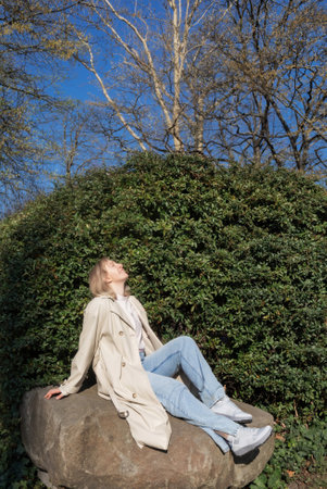 happy womam sitting on big stone in spring parkの写真素材