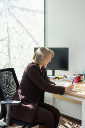 woman in suit writing at desk in officeの写真素材