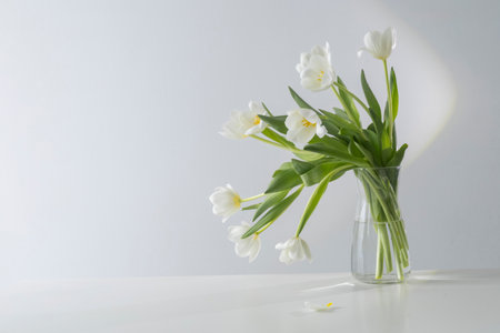 white tulips in glass vase in white interiorの写真素材