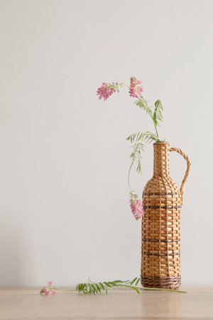 pink wild flowers in wicker bottle on light wooden tableの写真素材
