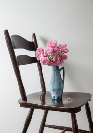 pink roses in blue jug on vintage wooden chair on background white wallの写真素材