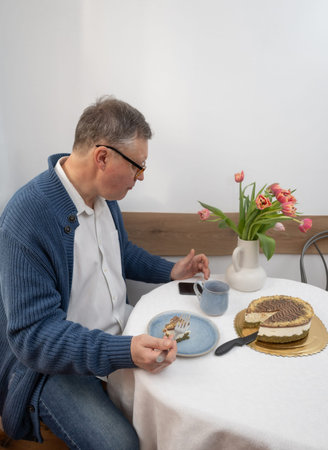 an elderly man eating a cake with smartphone in his kitchenの写真素材