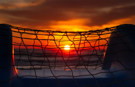 colorful blurred ocean sunrise seen through a fishing net on pedal boat at Rivazzurra (Rimini / Italy) beachの写真素材