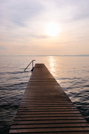 Wooden pier at sunset seen from walkway at Cisano, Bardolino, Lake Garda, Italy.の写真素材