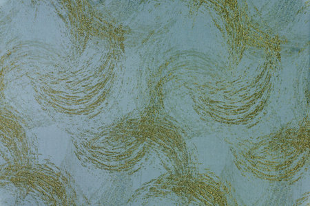 Teal and turquoise fabric background with a decorative golden wavy ornament. Woven material surface...