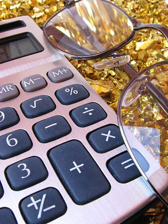 Calculator and glasses on interesting gold background made of small gold rocksの写真素材
