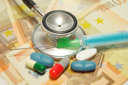 medical concept - health care costs - Stethoscope and syringe on money background and pillsの写真素材
