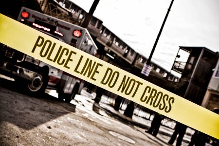 Yellow police tape with text: police line do not cross cornering off area from public access with blurred emergency vehicles in the backgroundの写真素材