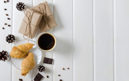 White cup of hot coffee with couple of croissants and chocolate. White wooden background.の写真素材