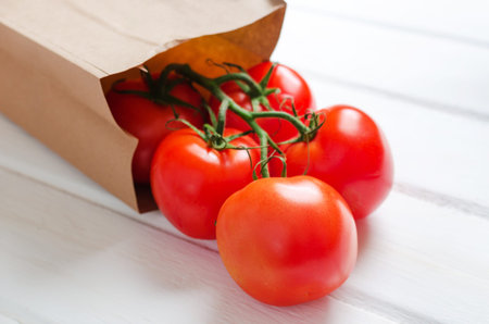 Tomato branch with paper bag on white wooden background. Close up.の写真素材