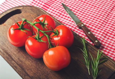 Branch of fresh ripe tomatoes on the wooden table with red checkered towel, healthy food. Toned.の写真素材
