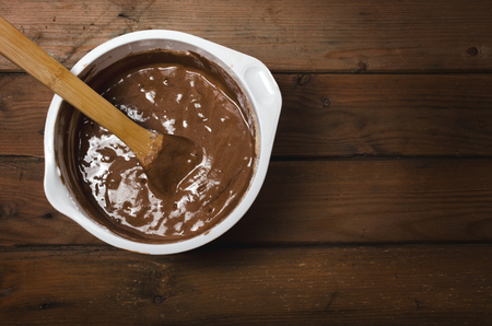 Cake pan with chocolate batter and wooden spoon close up on dark wooden background.の写真素材