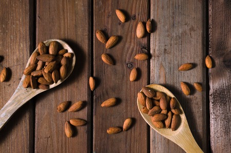 Almonds in a glass bowl and wooden spoons on grained wood background. Top view. Copy space.の写真素材