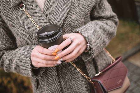 Cup of coffee in women's hands. Beautiful young brunette woman wearing grey coat. Autumn concept.