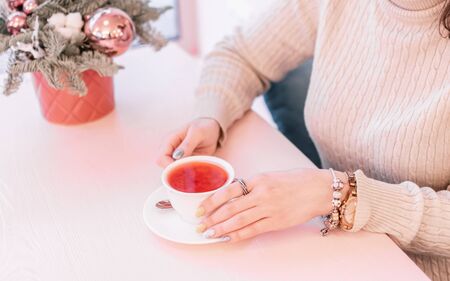 Close up of beautiful young woman s hands holding fruit hot tea cup at cafe shop. Selective focus.の写真素材