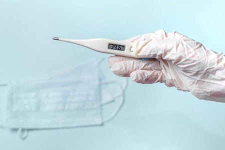 Medical mask for protection and hand holding thermometer on blue background. Against coronavirus and...