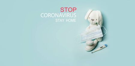 Medical masks with bunny toy and thermometer on blue background. Stop coronovirus text. Banner. Safe in home.の写真素材