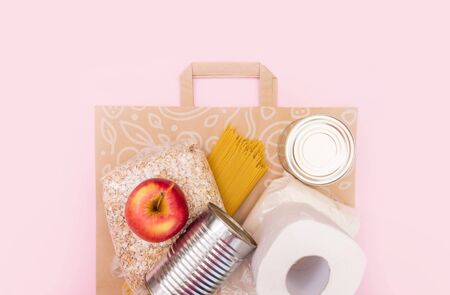 Food for quarantine isolation period flat lay on yellow background with copy space. Eggs, pasta, beans, toilet paper, apple and some seleals. Crisis food supplies. Delivery, donation concept.の写真素材