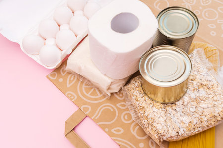Food for quarantine isolation period flat lay on yellow background with copy space. Eggs, pasta, beans, toilet paper, apple and some seleals. Crisis food supplies.の写真素材