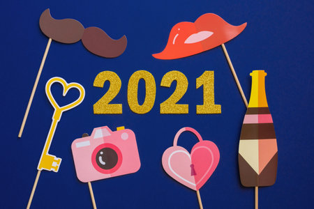 Happy New year 2021 celebration. Gold numeral 2021 on dark blue background and photo booth props.