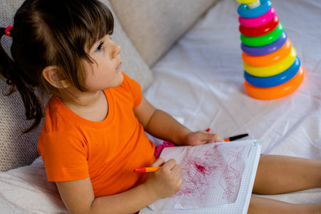 Little brown hair girl with brown eyes. 3 years old. Painting with pen in notebook.の写真素材