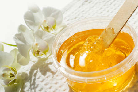 Sugar paste or wax honey in a transparent jar and white orchid on a white background. Sugaring. Depilation and beauty concept. Waxing.の写真素材