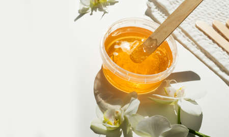 Sugar paste or wax honey in a transparent jar and white orchid on a white background. Sugaring. Depilation and beauty concept. Waxing.の写真素材