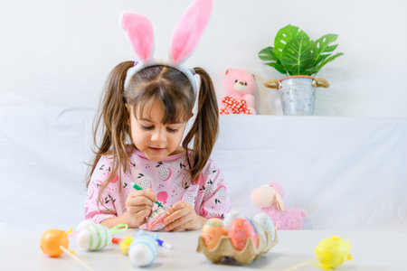 Happy little girl with bunny ears painting the egg with fiberpen, preparing for Happy Easter day....