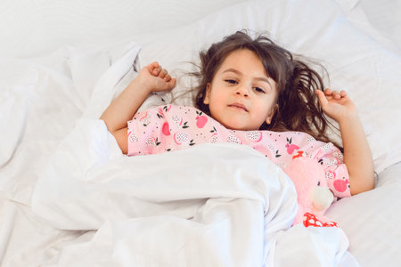 Angry dark hair girl sleeping sweetly in the morning on wihte bed linens at home. Childrens dreams,...