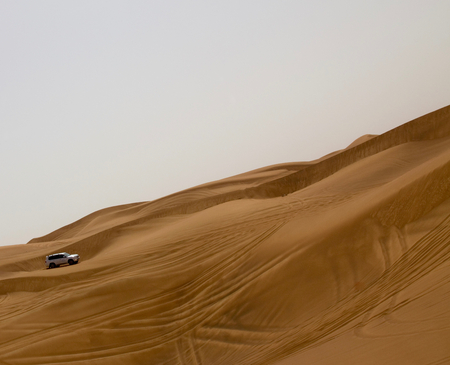 A car (SUV) trying to go up a steep slope in a desert in Dubai, UAEの写真素材