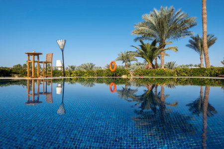 Swimming pool with clear blue water, palm trees and blue sky. Summer luxury resort. Ripple water...
