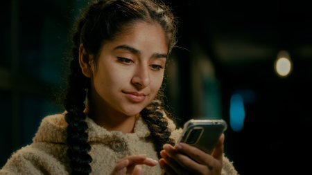 Arabian concentrated girl consumer shopper user young brunette middle-eastern woman stand in evening city texting messages on mobile phone gadget shopping online booking delivery scroll internet newsの写真素材