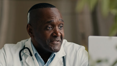 African doctor psychotherapist middle-aged man general practitioner talking with patient online video call in conference virtual webcam chat app medic consulting remote during corona virus pandemicの写真素材