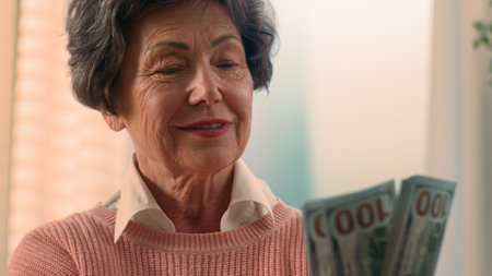 Happy smiling rich Caucasian old woman count money at home bills winning bonus grandmother counting dollars senior granny holding cash old female elderly retired lady with banknotes financial savingsの写真素材