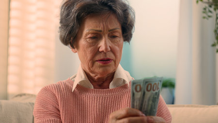 Sad dissatisfied stressed Caucasian old woman count money at home worry with debt world financial crisis bills grandmother counting fake dollars senior old female retired lady upset banknotes cashの写真素材