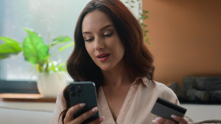 Satisfied Caucasian woman credit card holder use mobile app bank phone to pay online buy consumer girl at home buying goods order ecommerce websites booking food delivery safe transaction e-bankの写真素材
