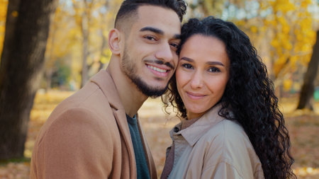 Close-up portrait outdoors Hispanic ethnic multiracial couple in love in autumn park looking at camera guy man and girl woman smiling stand close to each other touching heads lovers on romantic dateの写真素材