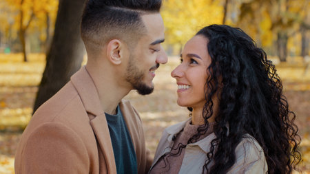Multiracial ethnic Hispanic happy married couple in love standing outdoors man and woman boyfriend and girlfriend wife and husband looking at each other with tenderness affectionate in autumn parkの写真素材