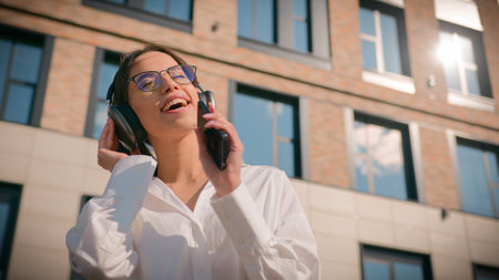 Happy asian woman businesswoman business lady female student listening music sing in headphones using mobile phone outdoors near office building joyful girl listen enjoy song singing moving dancingの写真素材