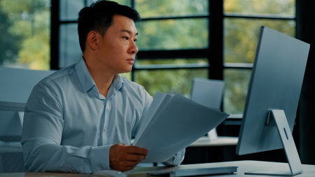 Professional asian businessman korean japanese 40s man lawyer office worker reading financial documents invoice contract budget documentation searching business data at computer paying bills onlineの写真素材