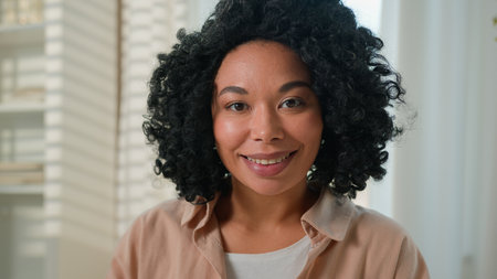 Close up portrait African American ethnic woman happy smiling girl beautiful millennial lady curly hairstyle female housewife homeowner at own home domestic living room looking at camera joyful smileの写真素材