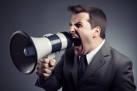 Young angry european businessman shouting to megaphone phone business man manager makes loud announcement adult male voice advertisement ad screaming microphone mouth speech anger furious personの素材