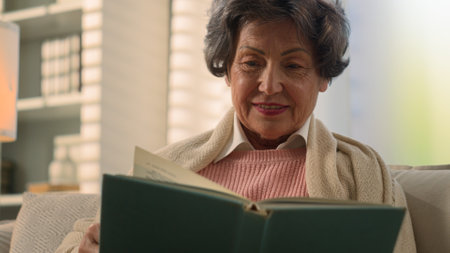 Happy inspired Caucasian old woman reading book smiling nostalgic senior mature lady elderly female retired pensioner grandmother read at home couch watching photos in album memory remember nostalgiaの写真素材