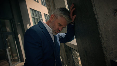 Exhausted stressed tired mature business man dizziness vertigo leaning wall of office company...