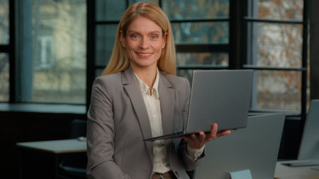 Middle-aged adult female CEO worker woman executive entrepreneur employee with laptop typing work posing for business portrait with smile. 40s Caucasian businesswoman working online smiling to cameraの写真素材