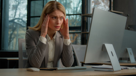 Sick ill sad Caucasian middle-aged adult woman mature business lady businesswoman worker employer in office with computer suffer with headache pain ache painful head stress migraine pressure sicknessの写真素材