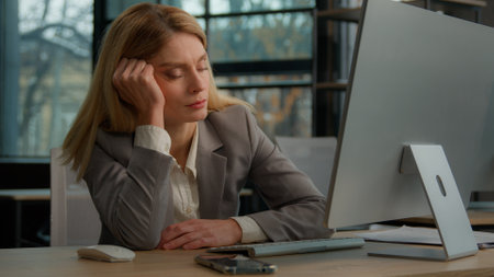 Tired sleeping exhausted napping businesswoman middle-aged Caucasian adult woman overworked employer female entrepreneur sleep sit at office desk workplace answer call talking phone typing computerの写真素材